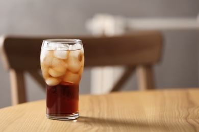 Glass of cola with ice on table against blurred background, space for text