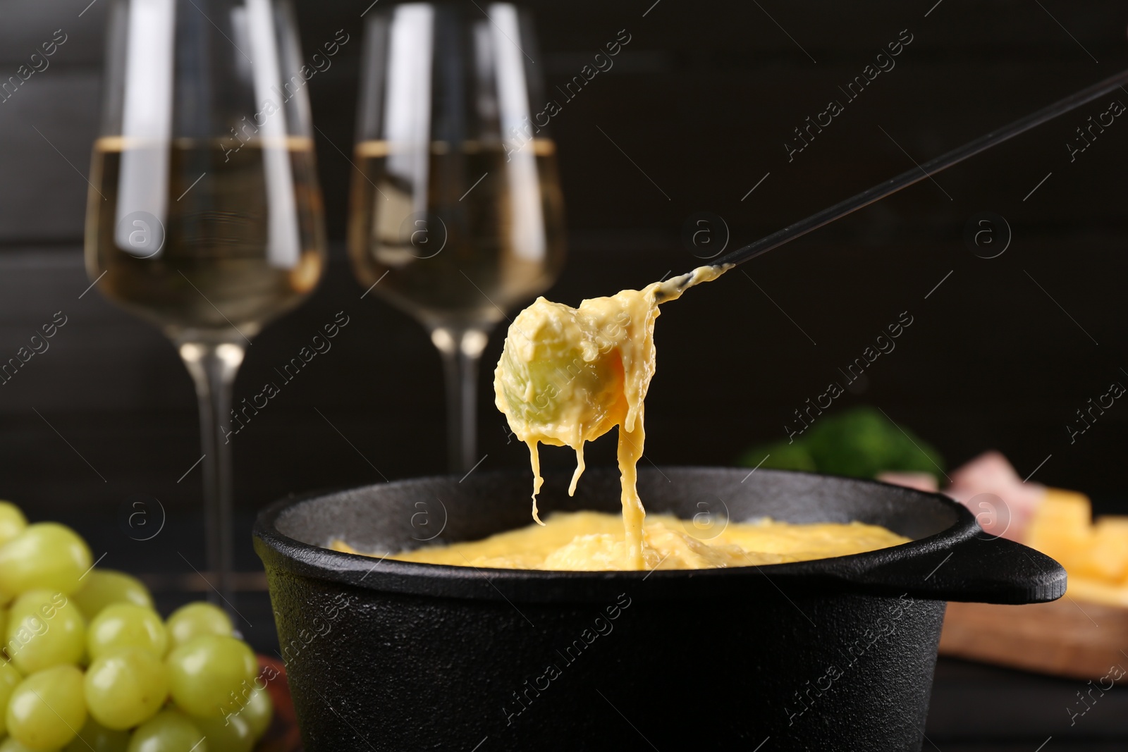 Photo of Dipping grape into fondue pot with melted cheese on table, closeup