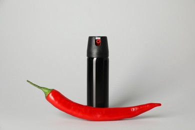 Photo of Bottle of gas spray and fresh chili pepper on grey background