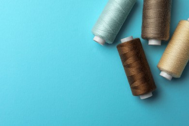 Photo of Different colorful sewing threads on light blue background, flat lay. Space for text