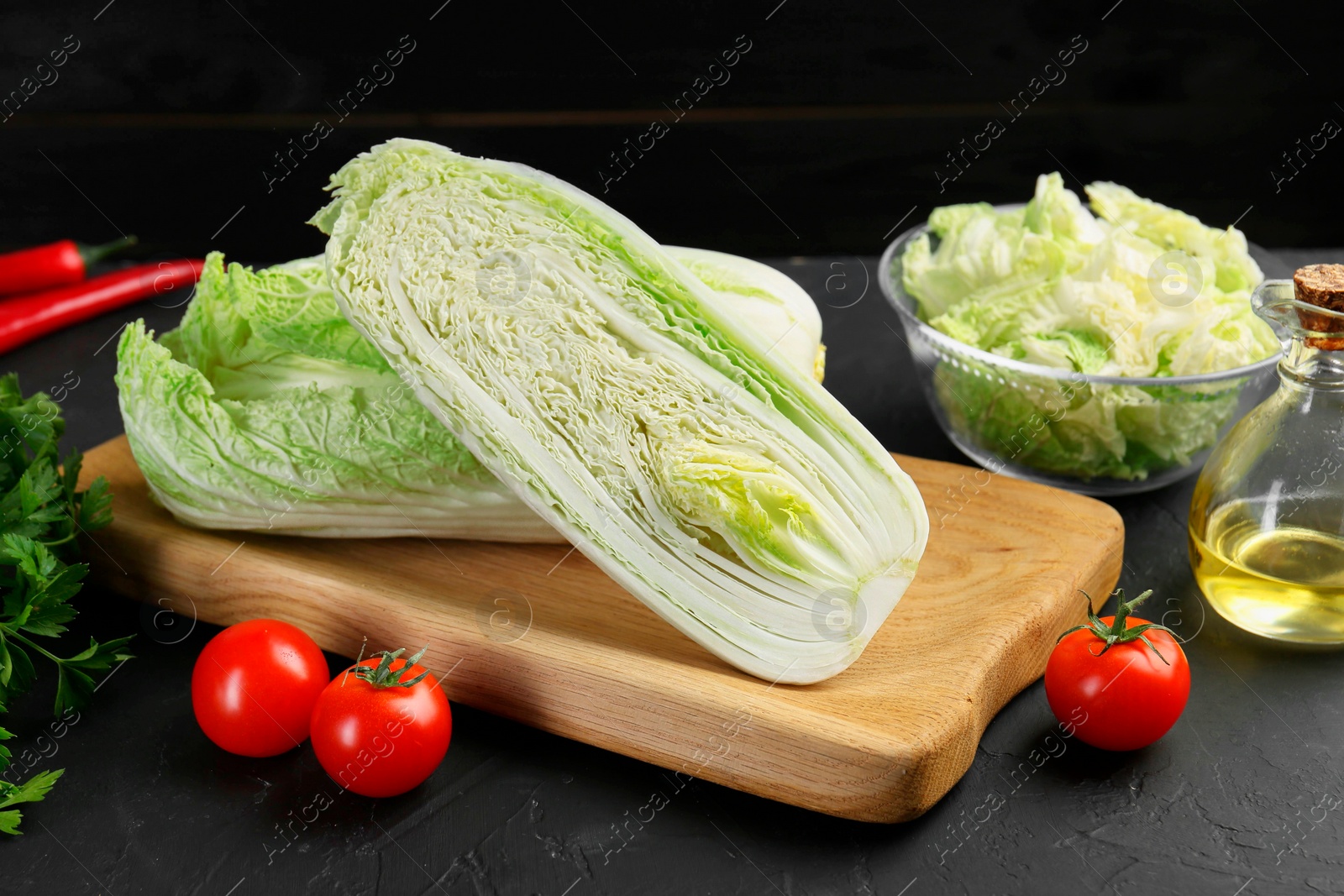 Photo of Fresh Chinese cabbages, tomatoes and oil on black textured table