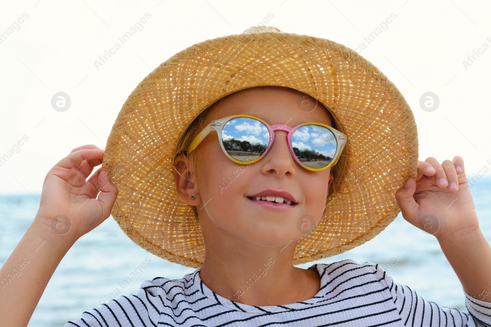 Photo of Little girl wearing sunglasses and hat at beach on sunny day