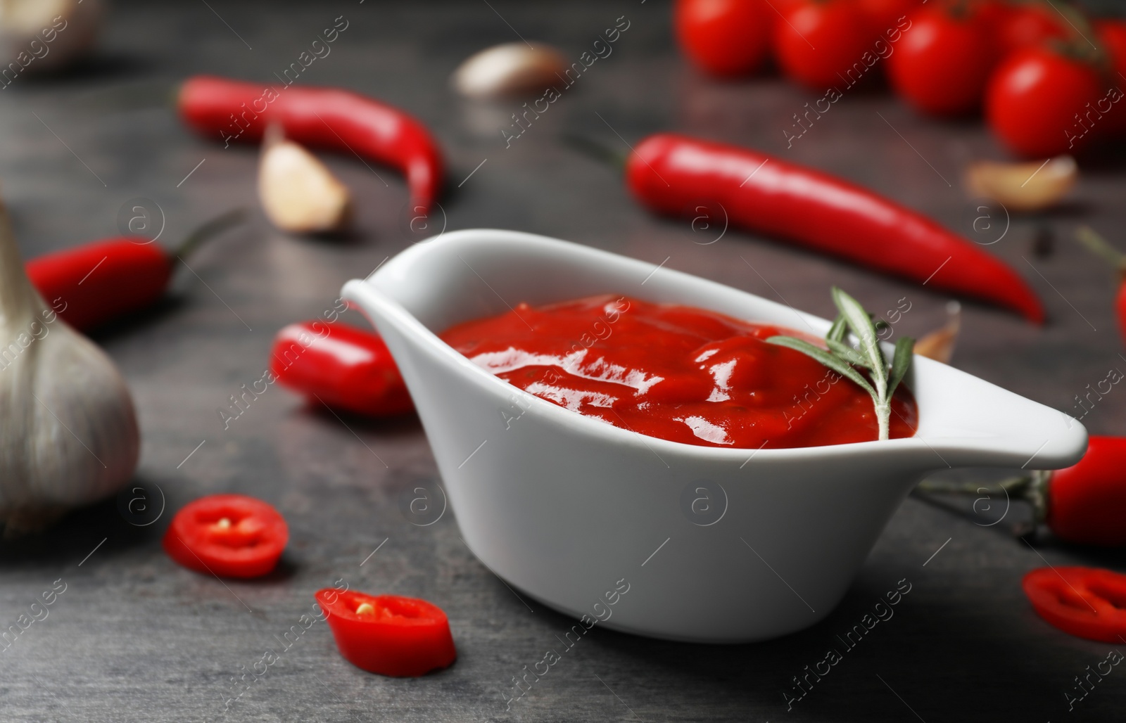 Photo of Gravy boat with hot chili sauce on gray table