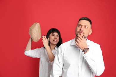 Photo of Woman popping paper bag behind her friend's back on red background. April fool's day