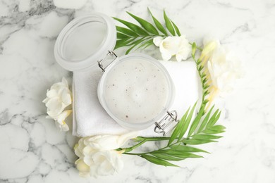 Photo of Jar of salt scrub, freesia flowers and towel on white marble table, flat lay