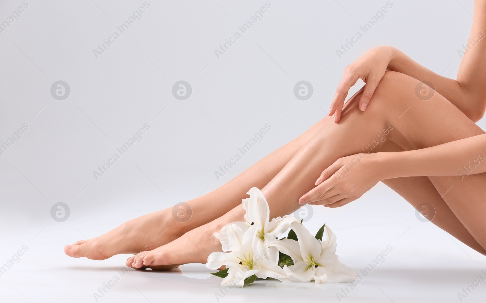 Photo of Young woman with silky skin and flowers on light background, closeup of legs