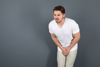 Photo of Young man with urological problems suffering from pain on grey background