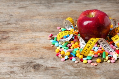 Photo of Weight loss pills with apple and measuring tape on wooden background. Space for text