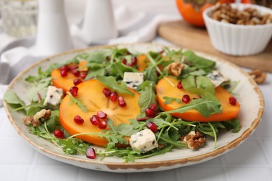 Tasty salad with persimmon, blue cheese, pomegranate and walnuts served on white tiled table, closeup