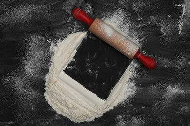 Photo of Flour and rolling pin on black table, top view. Space for text