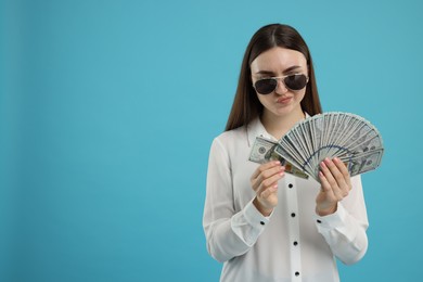 Photo of Woman with dollar banknotes on light blue background, space for text