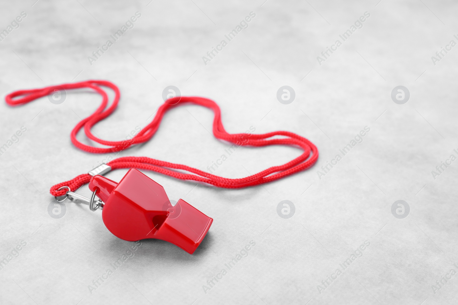 Photo of One red whistle with cord on light grey table. Space for text