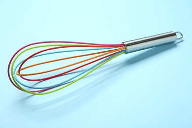 Photo of One whisk on light blue background, closeup