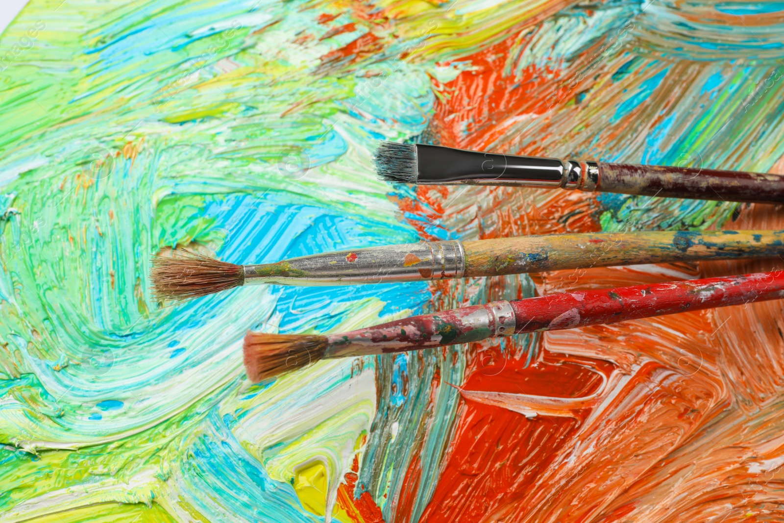 Photo of Closeup view of artist's palette with mixed paints and brushes as background