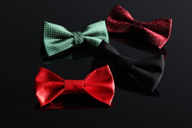 Photo of Stylish color bow ties on black mirror surface