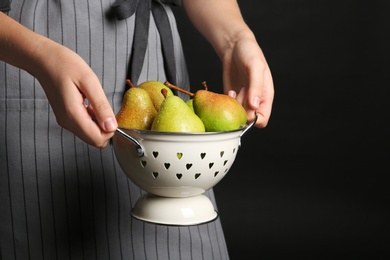 Woman holding colander with ripe pears on black background, closeup. Space for text