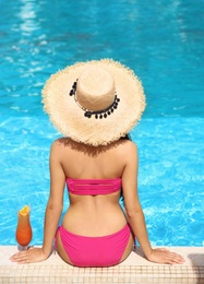Photo of Young woman with cocktail sitting near swimming pool