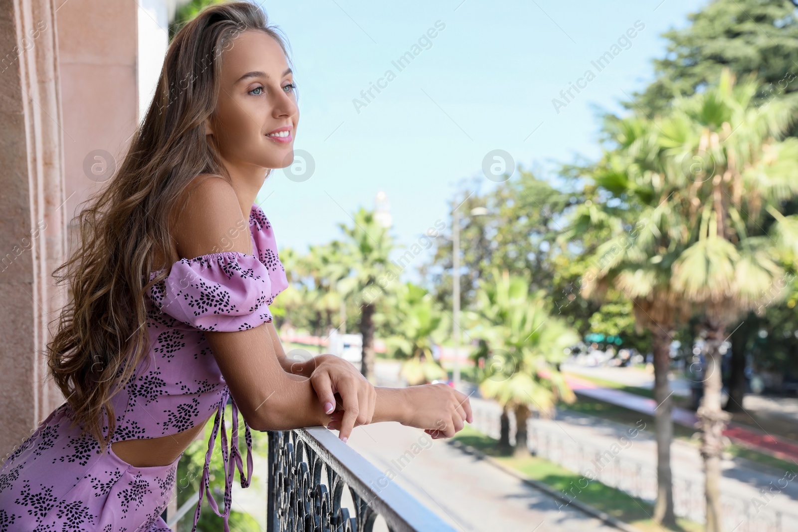 Photo of Beautiful young woman standing on balcony, space for text