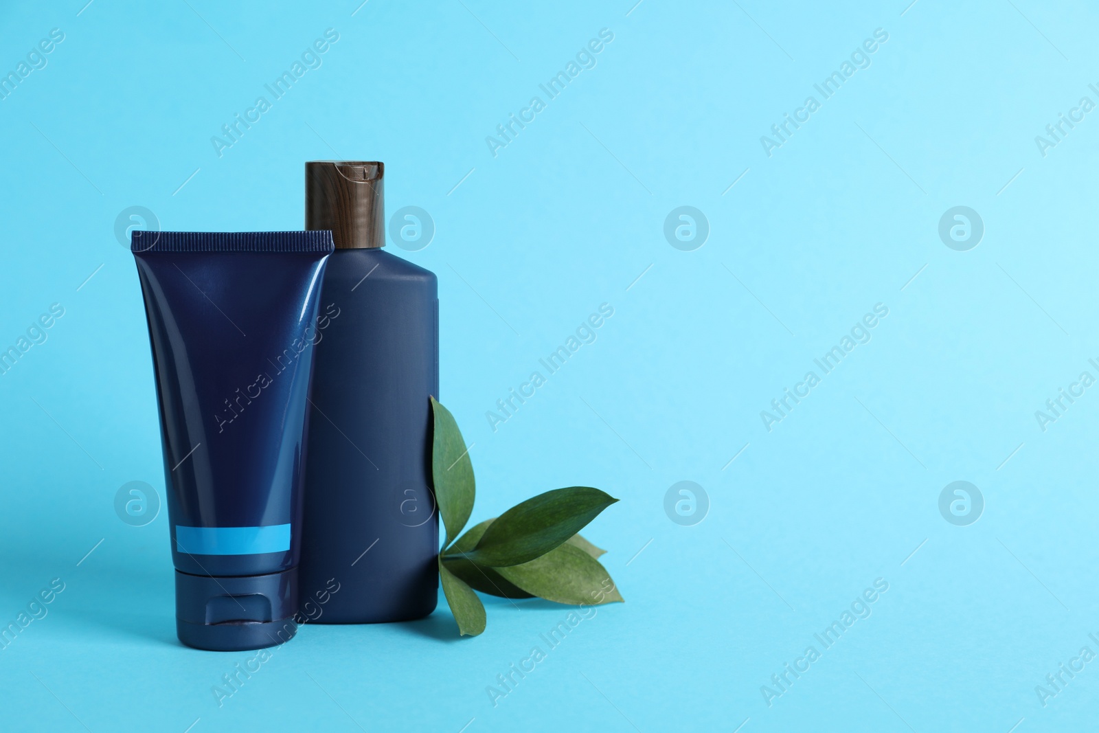 Photo of Men's facial cream, shampoo and green leaves on turquoise background. Mockup for design