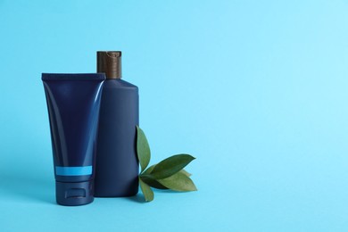 Men's facial cream, shampoo and green leaves on turquoise background. Mockup for design