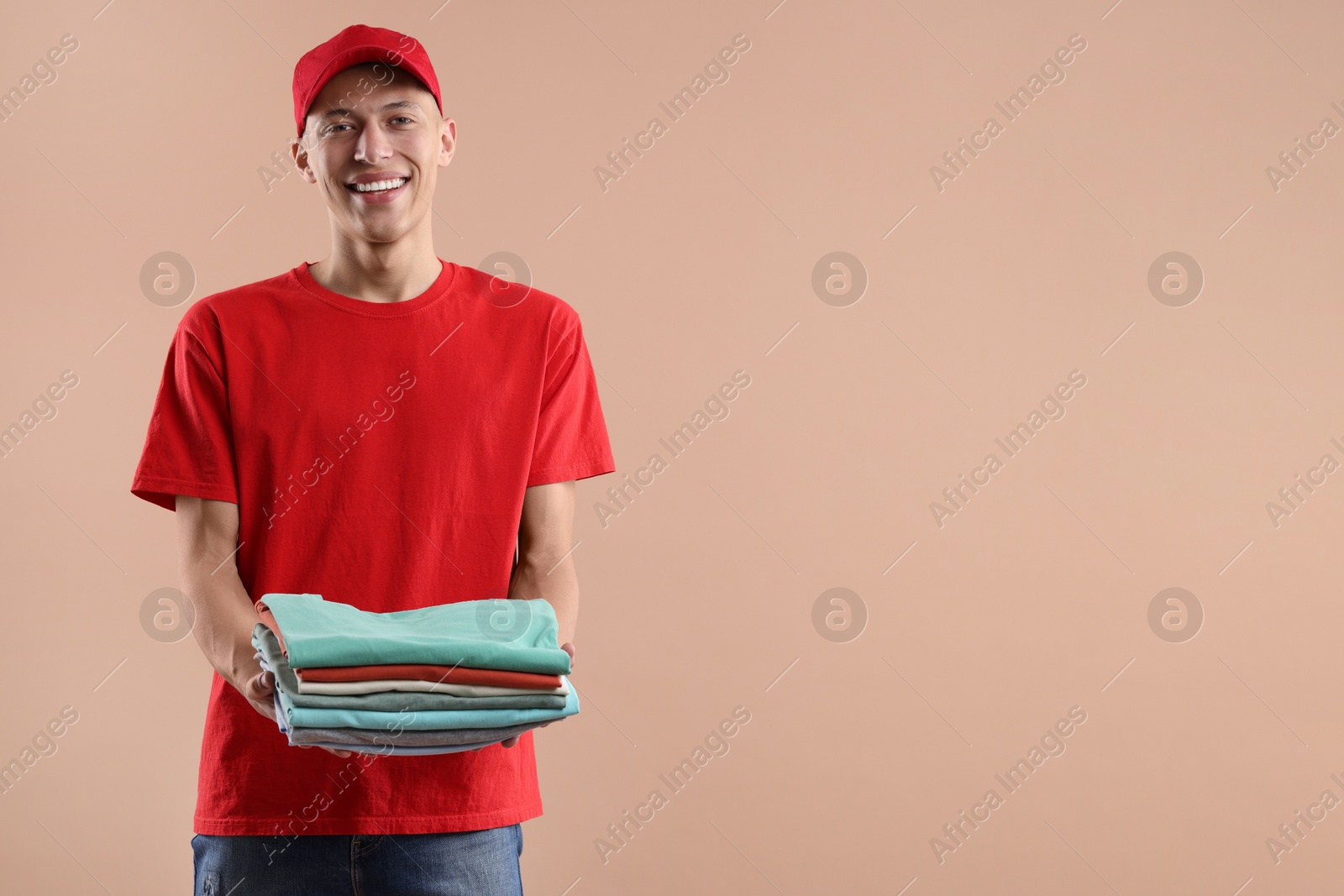 Photo of Dry-cleaning delivery. Happy courier holding folded clothes on beige background. Space for text
