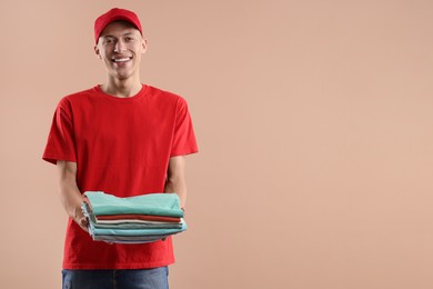 Dry-cleaning delivery. Happy courier holding folded clothes on beige background. Space for text