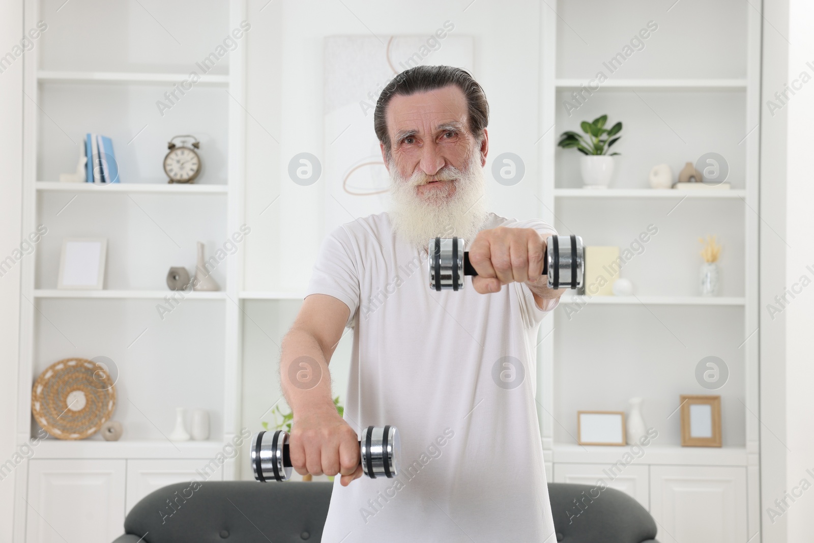 Photo of Senior man exercising with dumbbells at home. Sports equipment