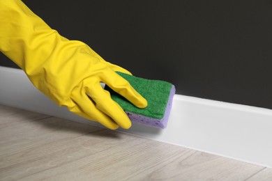 Photo of Woman in protective glove cleaning plinth with sponge indoors, closeup