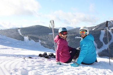 Photo of Happy couple with ski equipment sitting on snowy hill in mountains, space for text. Winter vacation