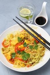 Photo of Stir-fry. Delicious cooked noodles with chicken and vegetables in bowl served on gray textured table, above view