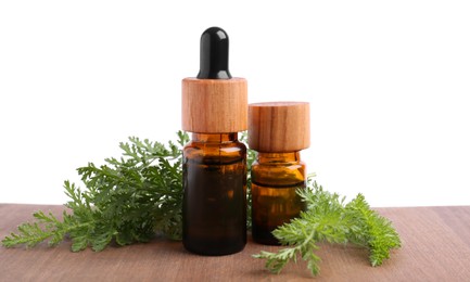 Photo of Bottles of essential oil and yarrow leaves on wooden table against white background