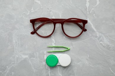 Photo of Case with contact lenses, tweezers and glasses on light grey marble table, flat lay