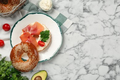 Photo of Delicious bagel with cream cheese, jamon, tomato and parsley on white marble table, flat lay. Space for text