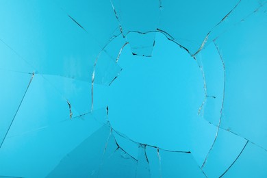 Photo of Closeup view of broken glass with cracks on light blue background