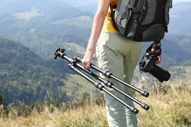 Photo of Woman with modern camera and tripod in mountains, closeup