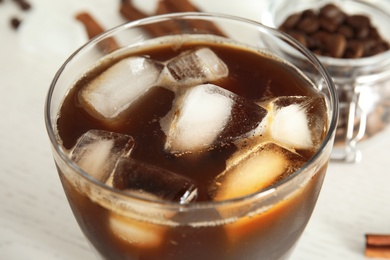 Glass of coffee drink with ice cubes on table, closeup