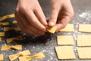 Woman making farfalle pasta at grey table, closeup