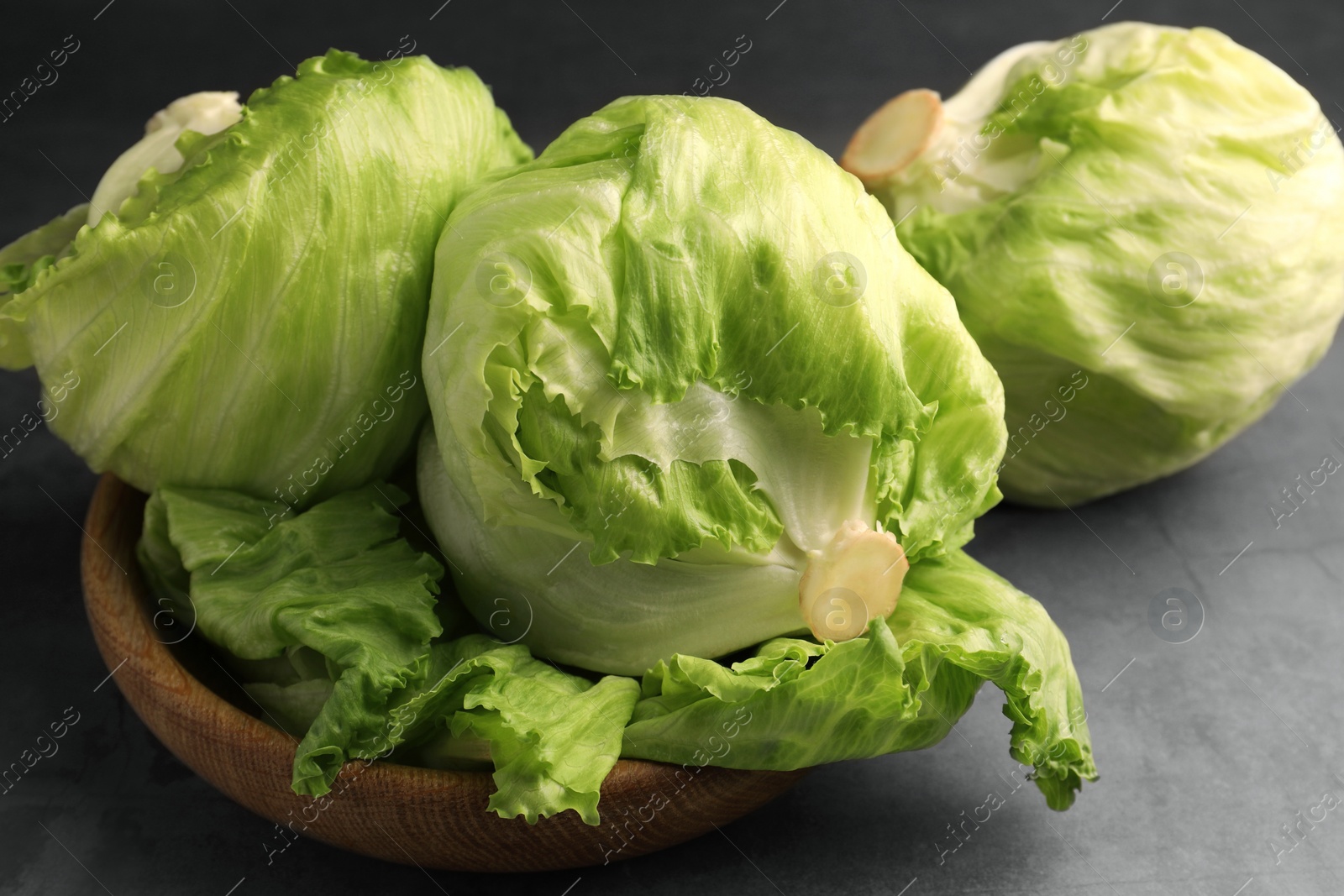 Photo of Fresh green iceberg lettuce heads and leaves on grey table, closeup