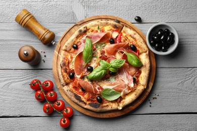 Photo of Tasty pizza with cured ham, olives, tomatoes and basil on gray wooden table, flat lay