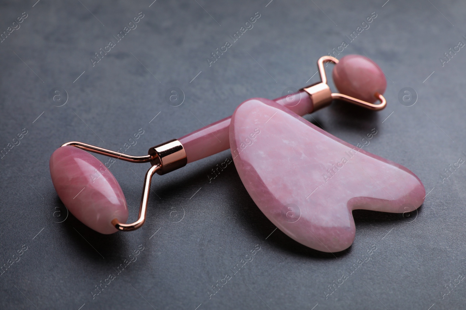 Photo of Quartz gua sha tool and face roller on grey table, closeup