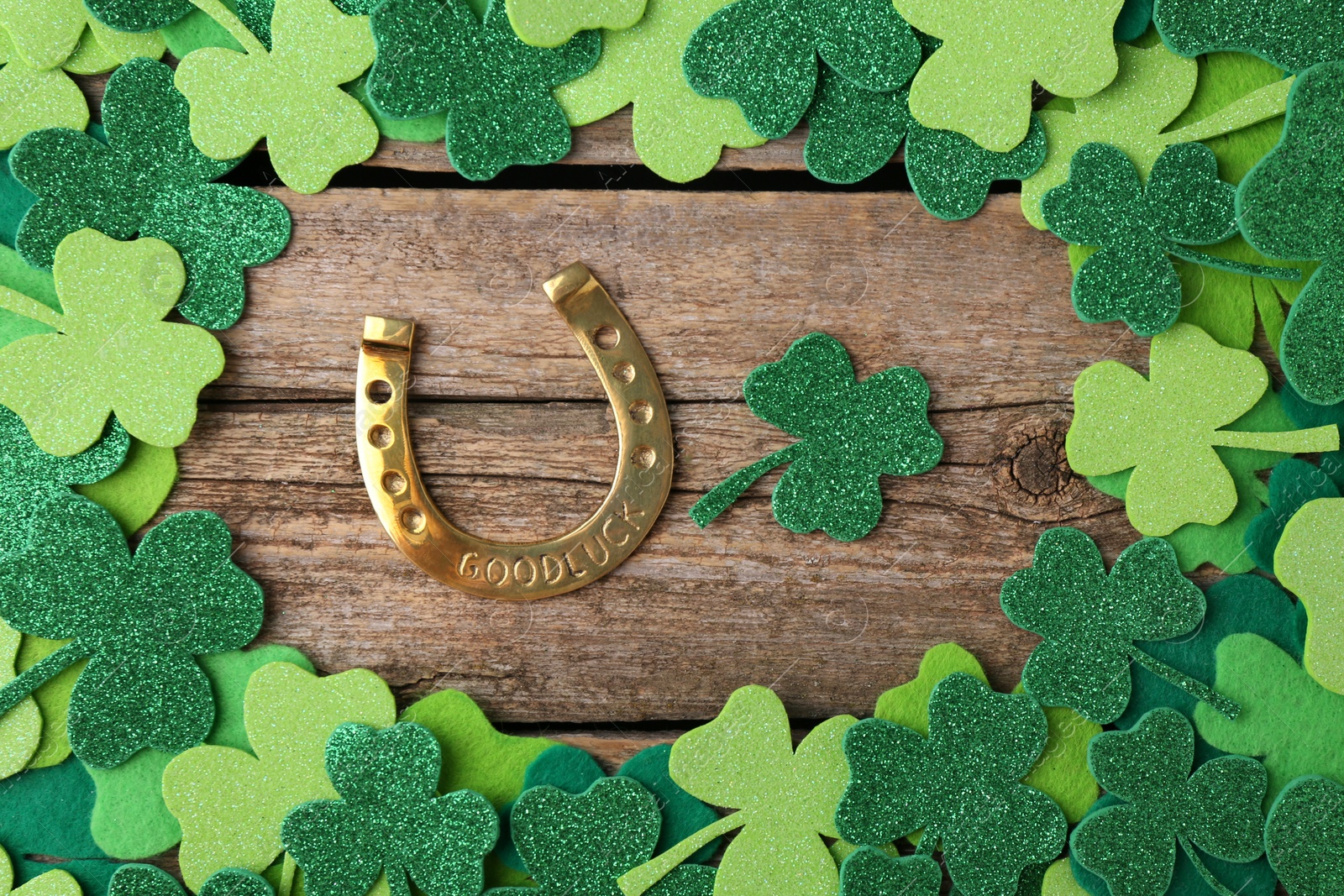 Photo of St. Patrick's day. Golden horseshoe and green decorative clover leaves on wooden table, flat lay