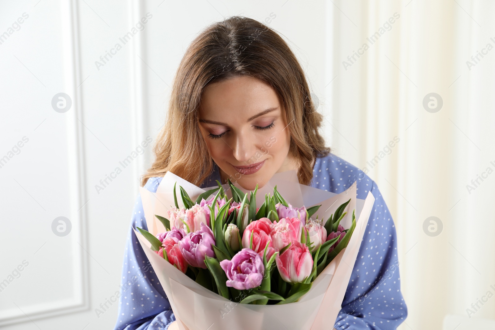 Photo of Happy young woman with bouquet of beautiful tulips indoors