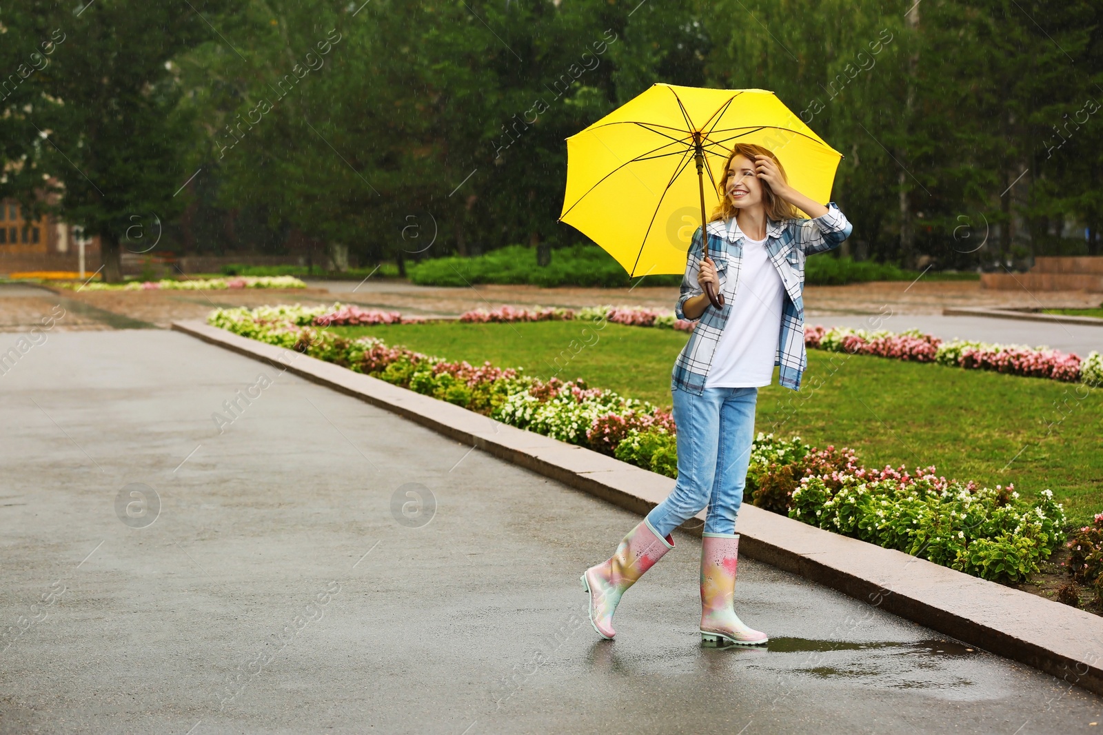 Photo of Happy young woman with umbrella under rain in park