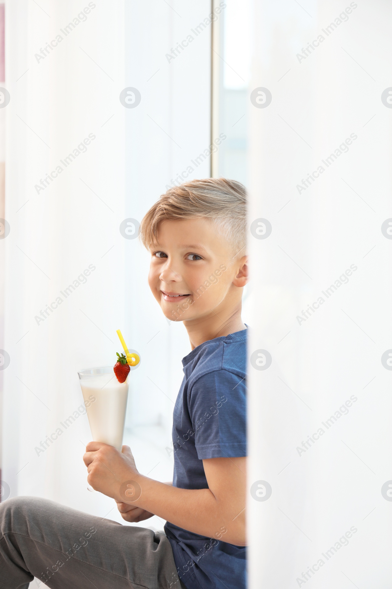 Photo of Little boy with glass of milk shake near window indoors