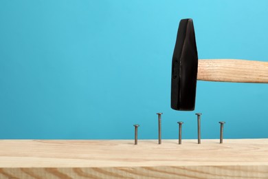 Photo of Hammering nail into wooden surface against light blue background, space for text