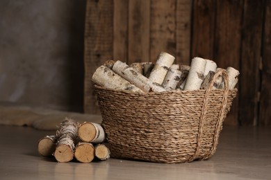 Photo of Wicker basket with cut firewood on floor indoors