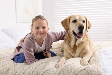 Photo of Cute child with her Labrador Retriever on bed at home. Adorable pet