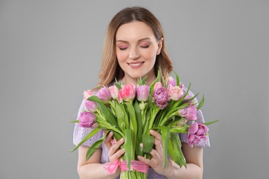 Photo of Happy young woman with bouquet of beautiful tulips on grey background
