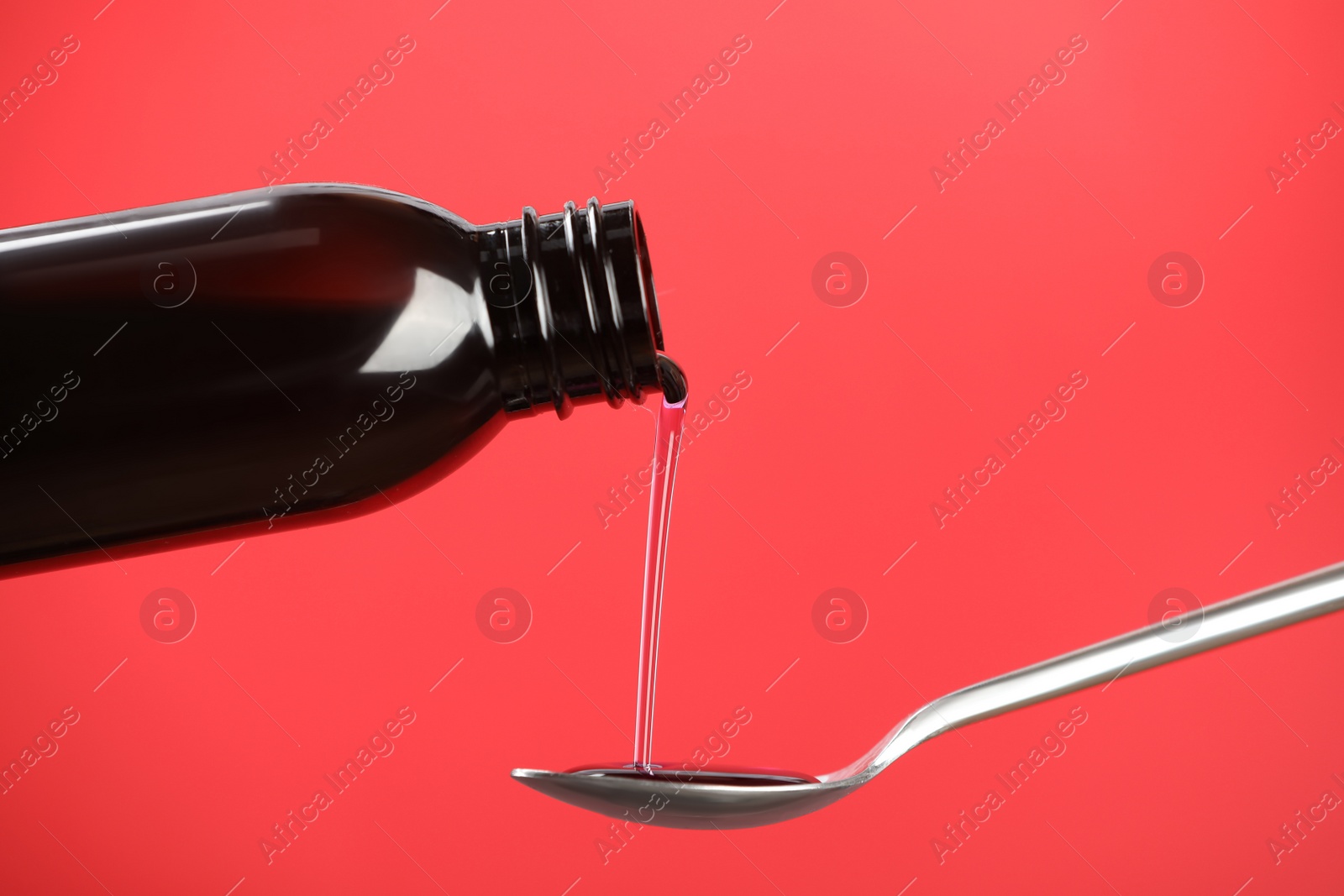 Photo of Pouring cough syrup into spoon on red background