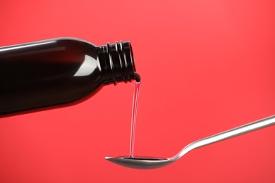 Pouring cough syrup into spoon on red background